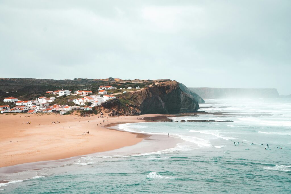 A scenic view of the cliff face and the town of Arrifana in the background, featuring the ocean where people are learning in Portugal surf