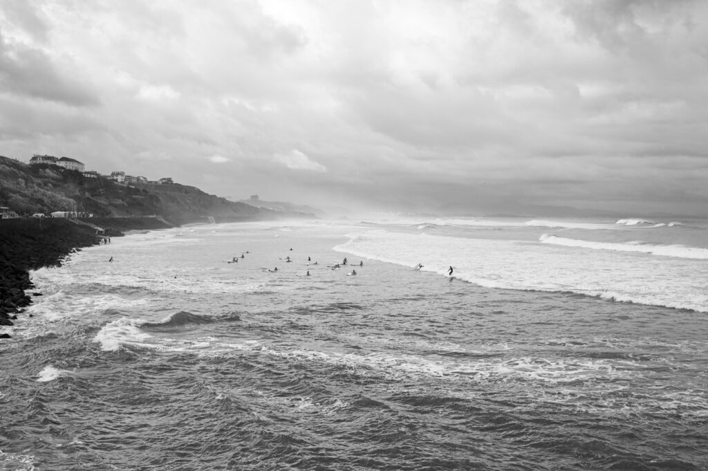 Black and white photo capturing the ocean in Biarritz surf, France, with people learning to surf