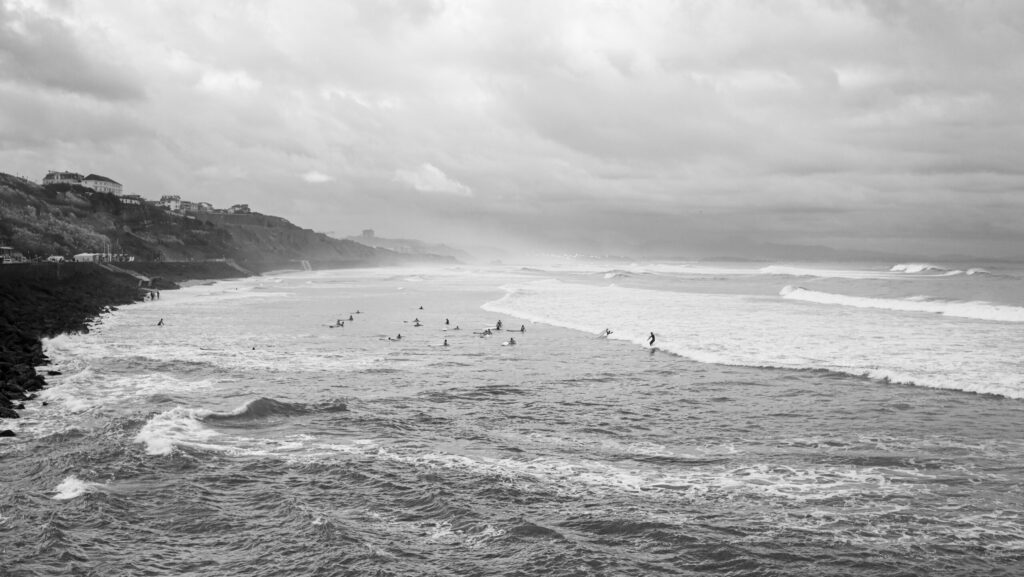Black and white photo capturing the ocean in Biarritz surf, France, with people learning to surf