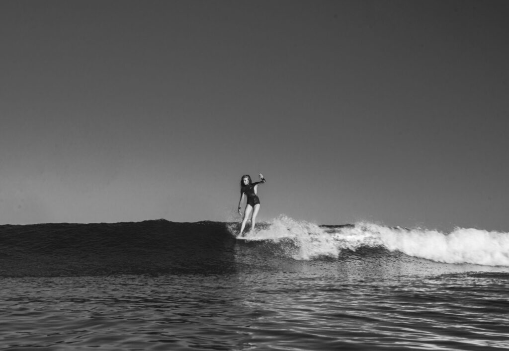 Black and white photo of a female surfer hanging five on a waist height, long right hand wave at First Point, Malibu surf, CA