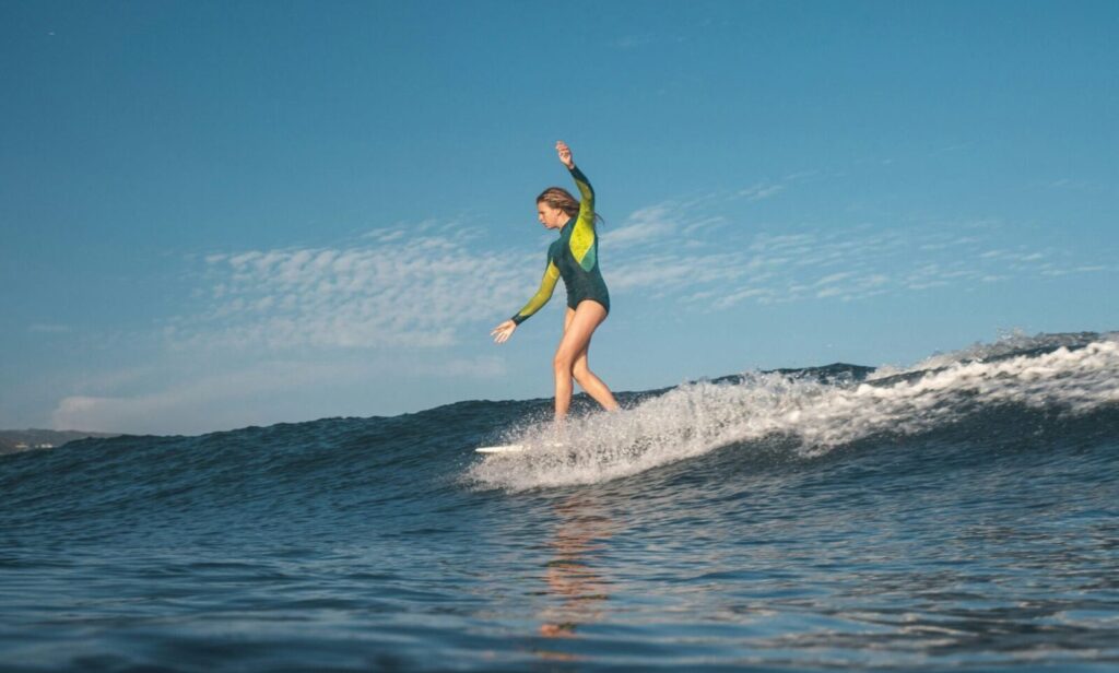 Water-level shot of a female surfer riding a mellow right-hand wave in Malibu surf, CA, dancing on her board under blue skies