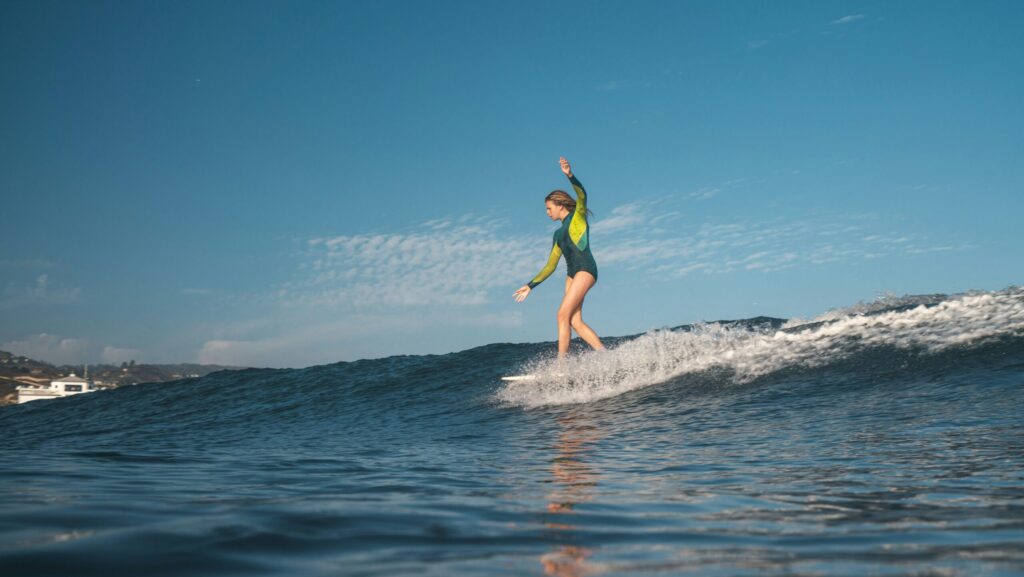 Water-level shot of a female surfer riding a mellow right-hand wave in Malibu surf, CA, dancing on her board under blue skies