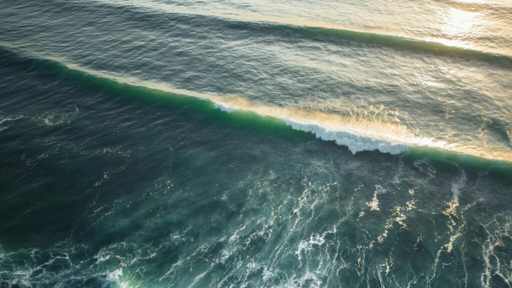 Aerial drone view of rolling waves in Peniche Surf, Portugal, with sunlight reflecting off the water