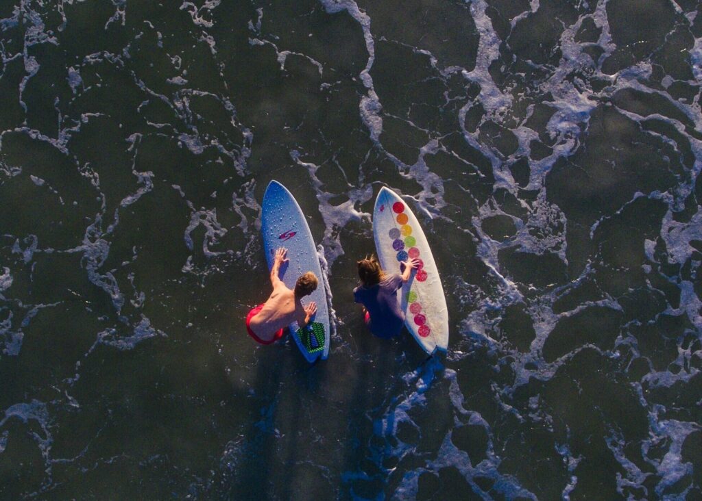 A bird's-eye view from a drone of two surfers holding their surfboards while standing in shallow water in Mancora surf