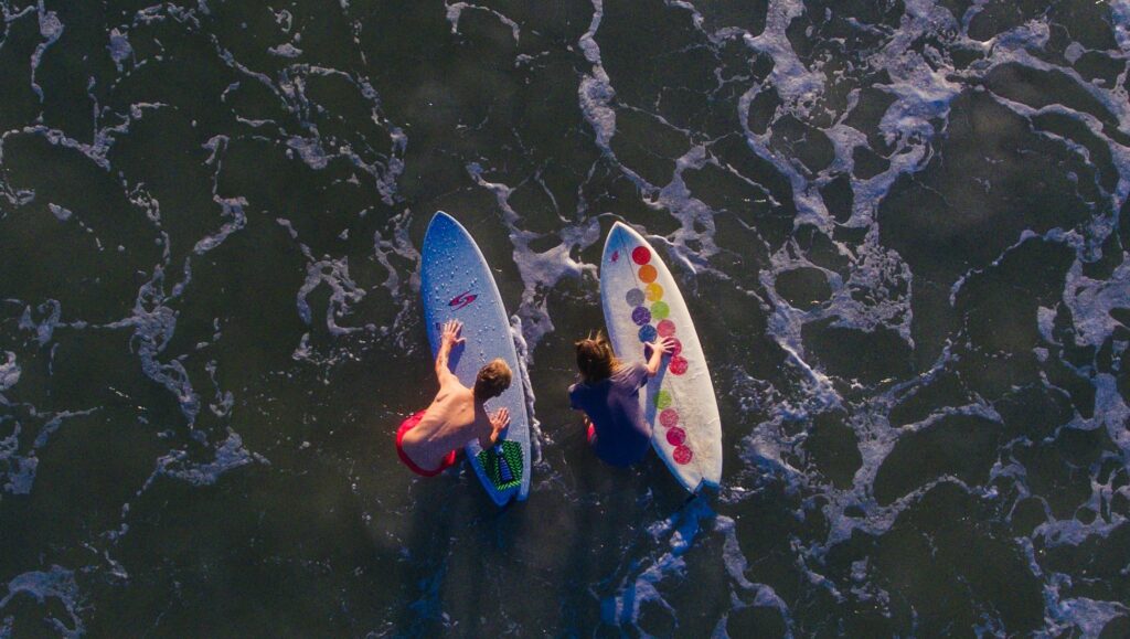 A bird's-eye view from a drone of two surfers holding their surfboards while standing in shallow water in Mancora surf
