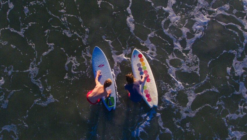 A bird's-eye view from a drone of two surfers holding their surfboards while standing in shallow water in Mancora surf