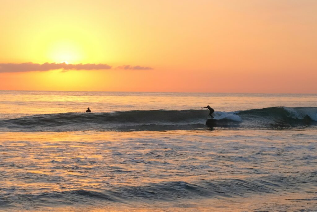 Surfer racing along a mellow right hand wave at Malibu Surf, CA, with a vibrant sunset and clear yellow-orange skies in the background