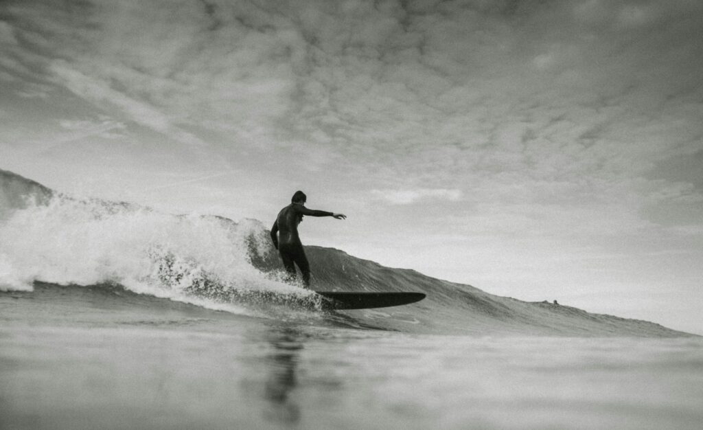 A man surfing a longboard on a gentle wave at Higgins Beach surf, Maine, under a clear sky with calm ocean waters in the background.