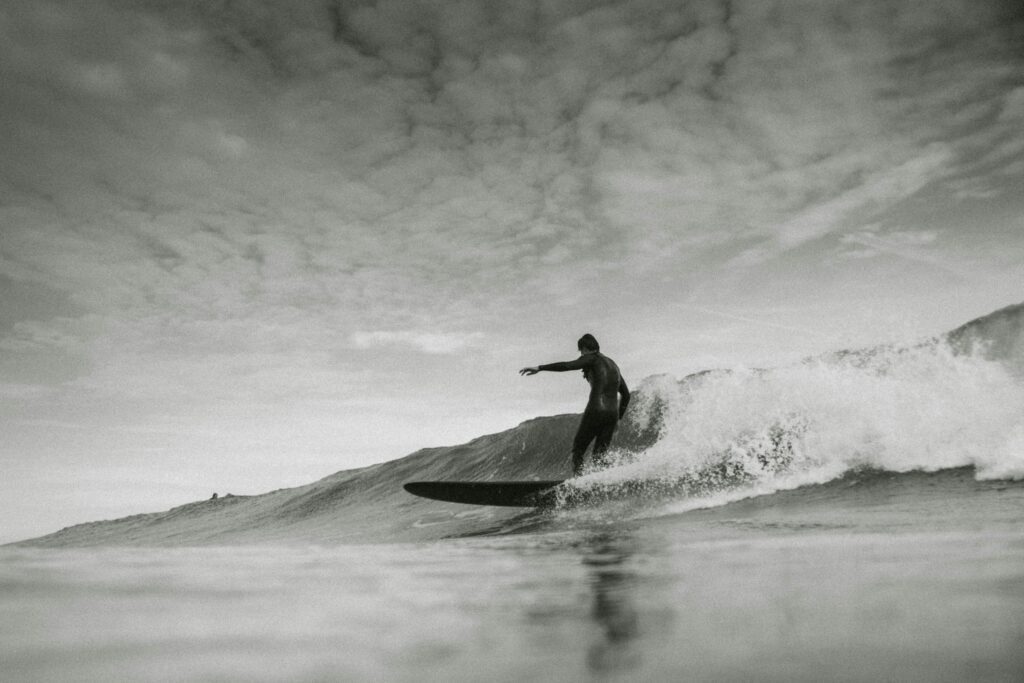 A black and white photo of a surfer on a longboard in Essaouira Surf, captured from the wave, riding a rolling left-hand wave