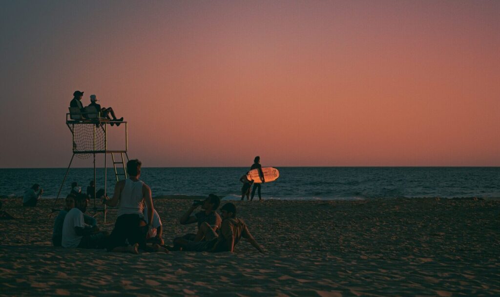 A sunset image featuring pink and blue skies, with people enjoying the beach