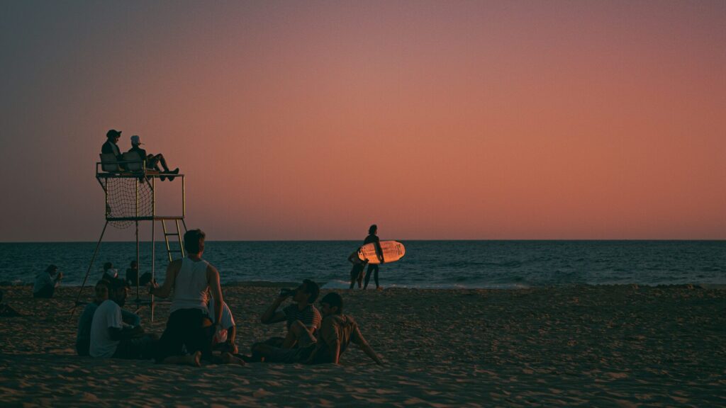 A sunset image featuring pink and blue skies, with people enjoying the beach