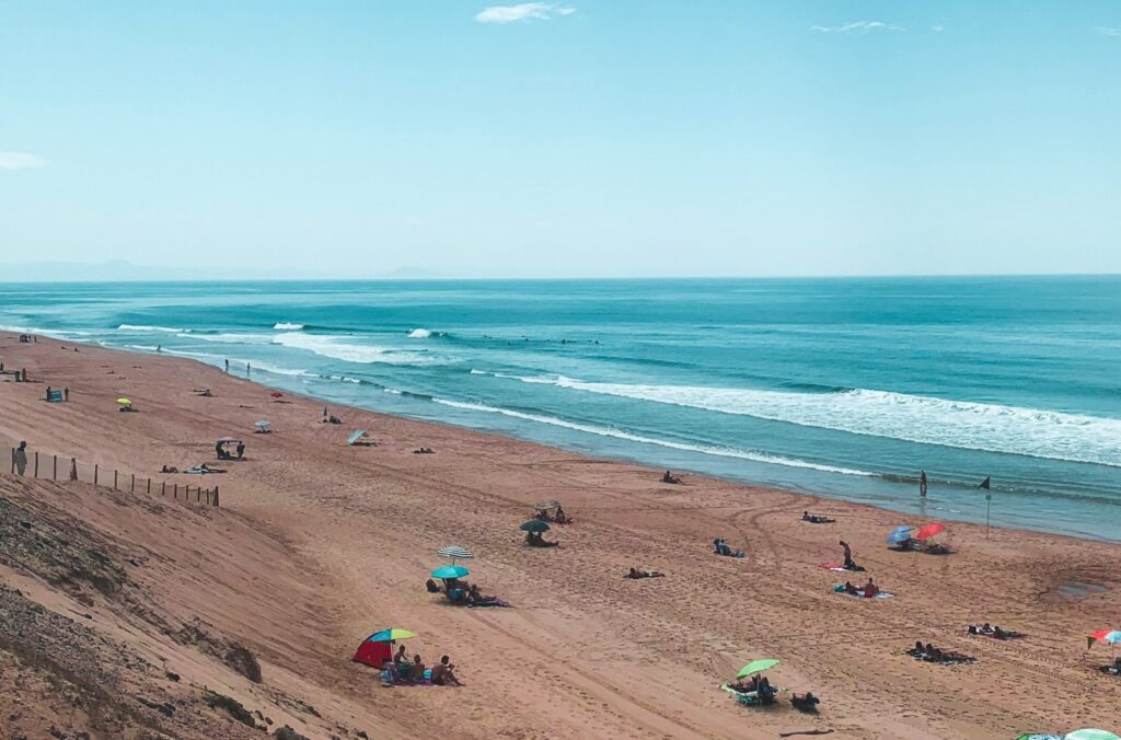 The ocean in Capbreton surf, France, features sandy shores and vibrant blue water under clear blue skies, with people relaxing on the beach