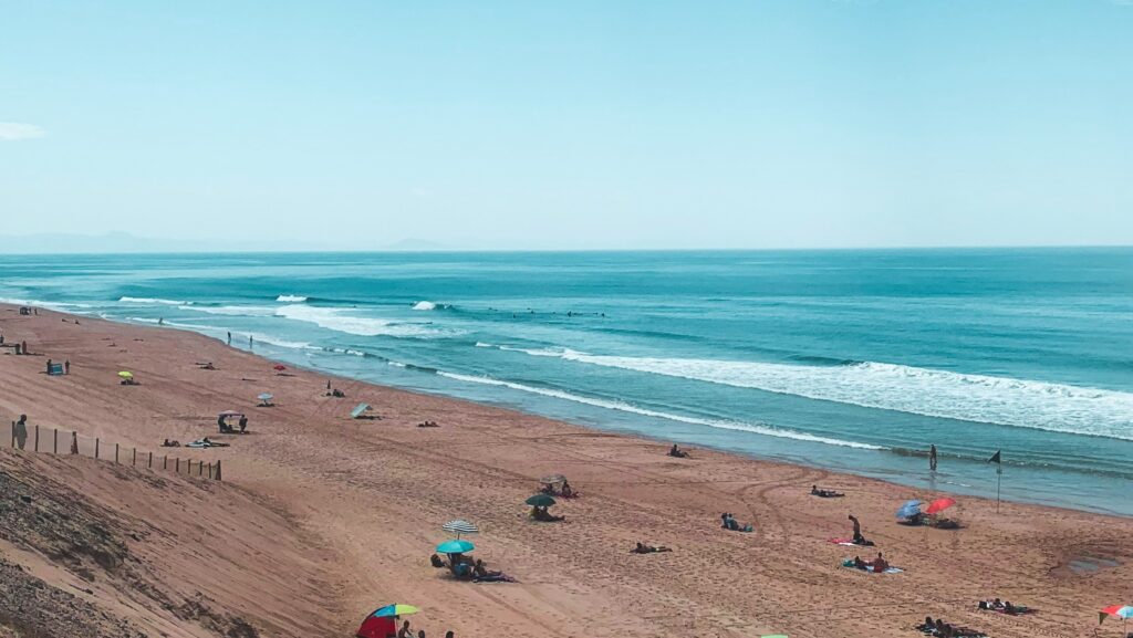 The ocean in Capbreton surf, France, features sandy shores and vibrant blue water under clear blue skies, with people relaxing on the beach