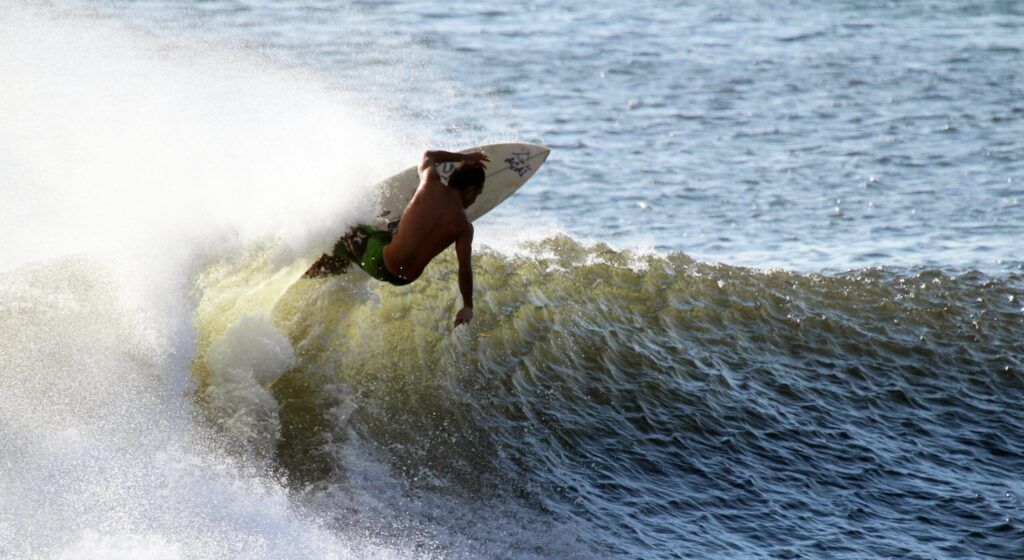 A surfer performing a powerful top turn on a left-hand wave at Cimaja Surf, skillfully carving through the water with spray flying around them