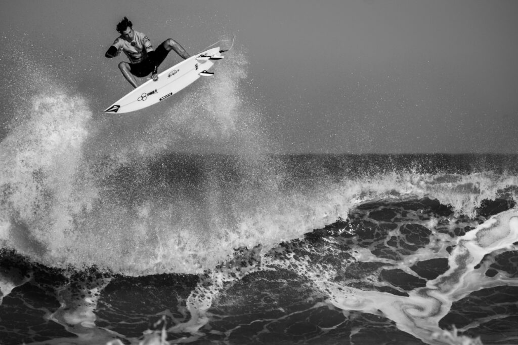 A surfer executing a huge aerial maneuver above the wave in Lacanau Surf, France, showcasing skill and style