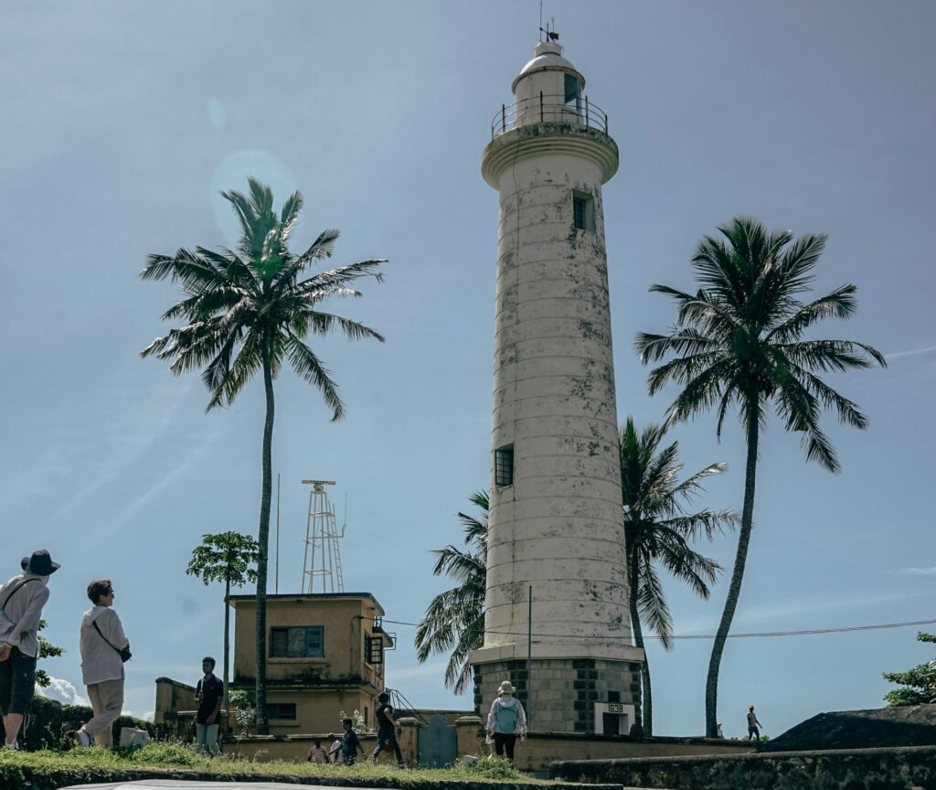 White lighthouse at Galle with people observing and palm trees in the background