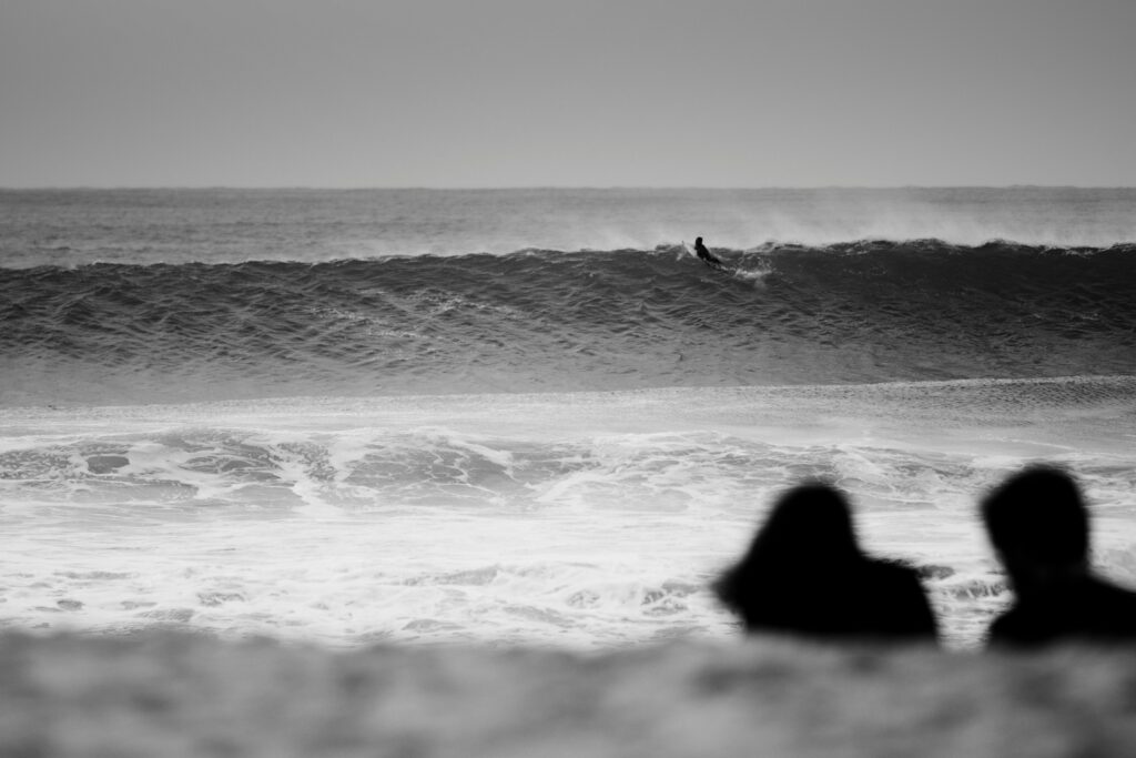 A black-and-white photo capturing a large right-hand wave, with a surfer paddling over the crest in Supertubos, Peniche Surf, Portugal