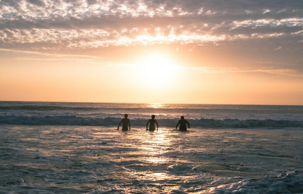 Three people entering the ocean at Waikiki Beach, Miraflores surf, Lima, with a stunning sunset and vibrant yellow skies