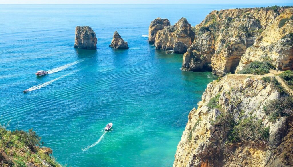 Cliffs and rocks of Lagos, Portugal, showcase clear blue water and blue skies, with boats