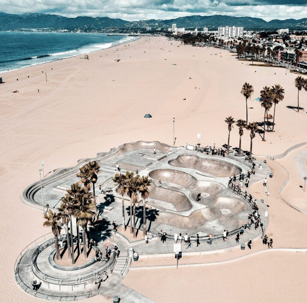 Drone shot of Venice Beach featuring the iconic Venice Skatepark, with buildings and sandy shoreline in the background