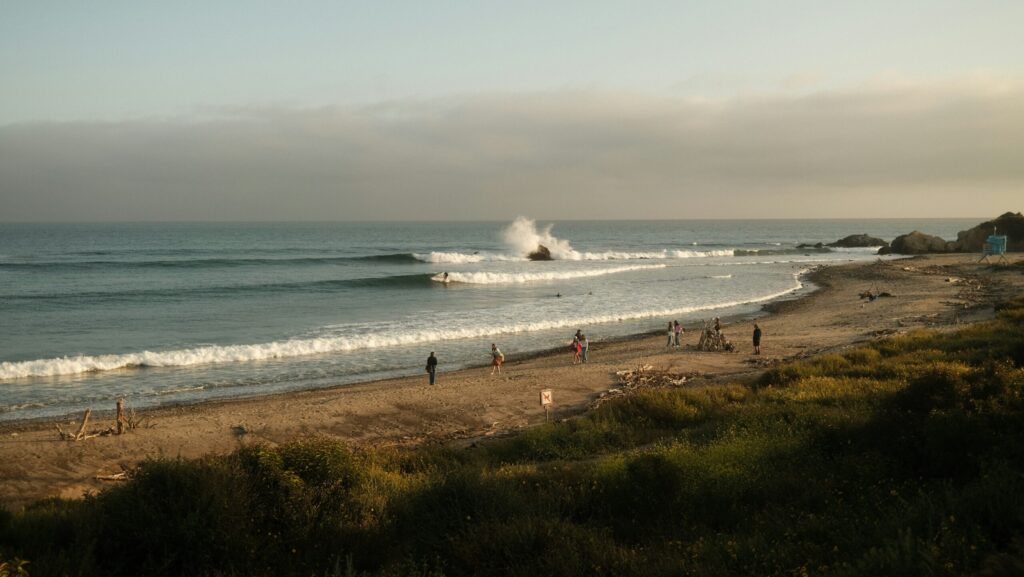 Long right hand waves at Malibu Surf in California with clear skies and people walking on the beach