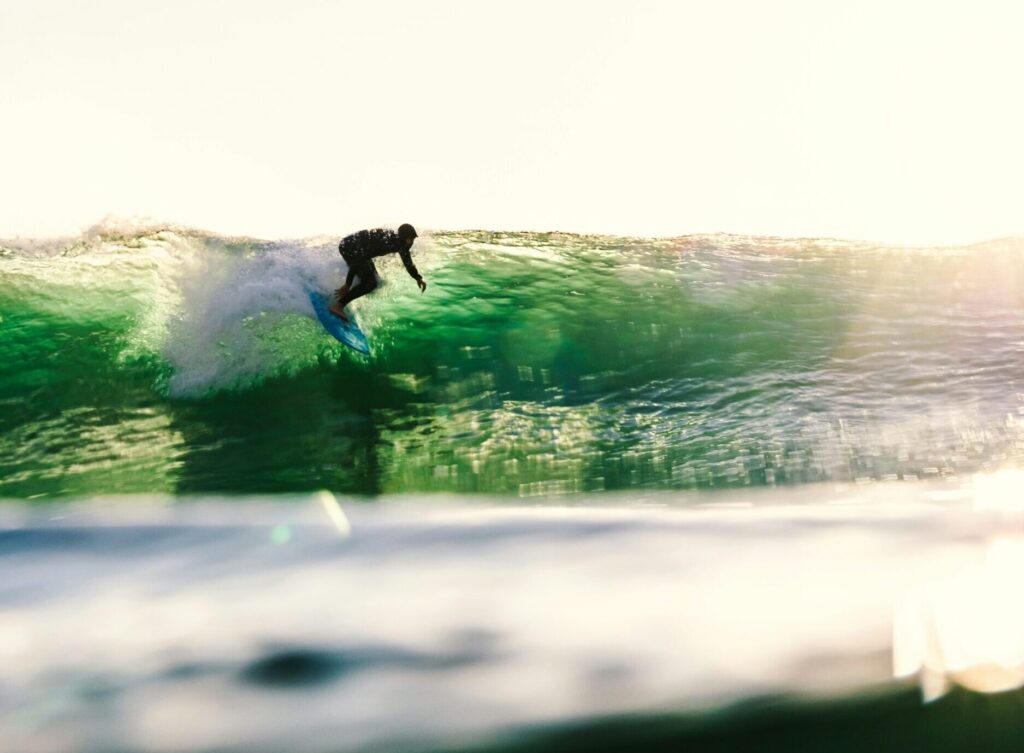 Surfer taking off on a green wave, looking down the line as the low sun reflects on the water at Sunset Cliffs surf, San Diego, California