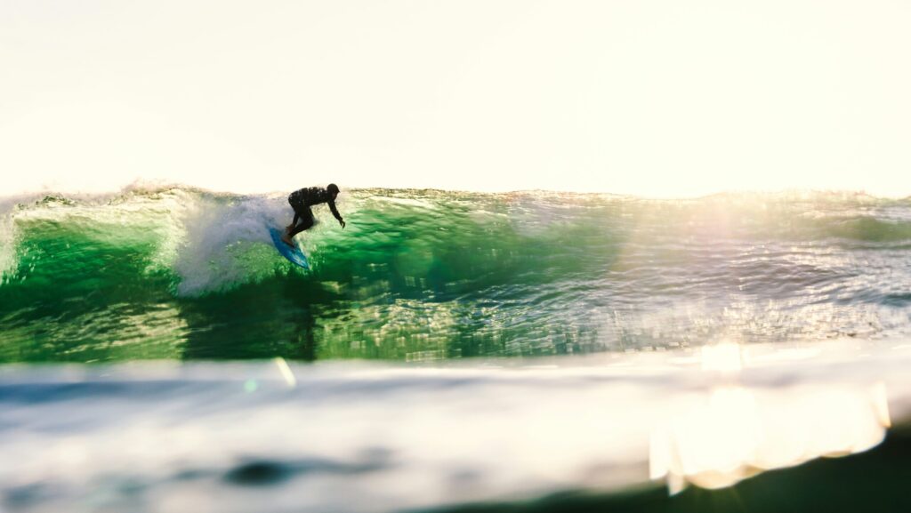 Surfer taking off on a green wave, looking down the line as the low sun reflects on the water at Sunset Cliffs surf, San Diego, California