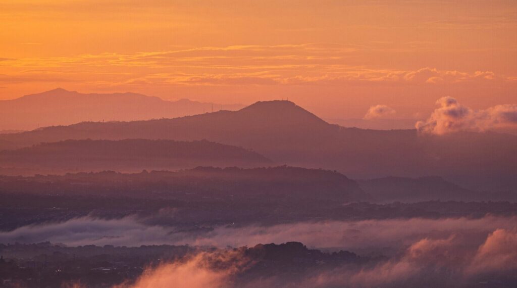 A scenic view of San Salvador, El Salvador, with a vibrant yellow-orange skyline, rolling hills, and a mix of low and high clouds