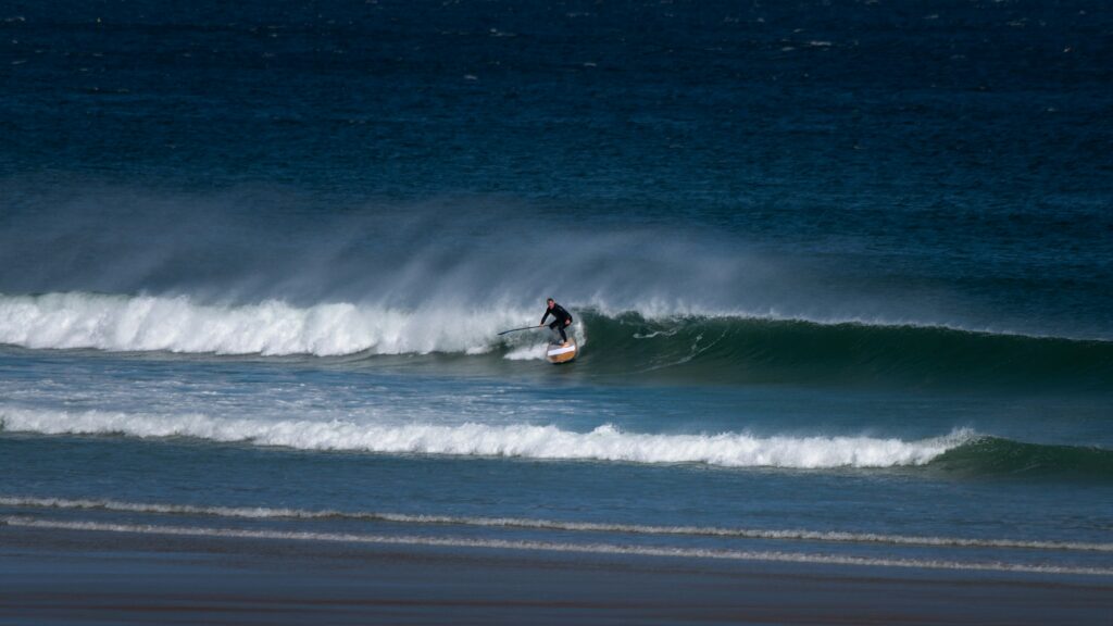 A man catching a left-hand wave on a stand-up paddleboard, riding the wave with strong offshore winds in Mancora surf