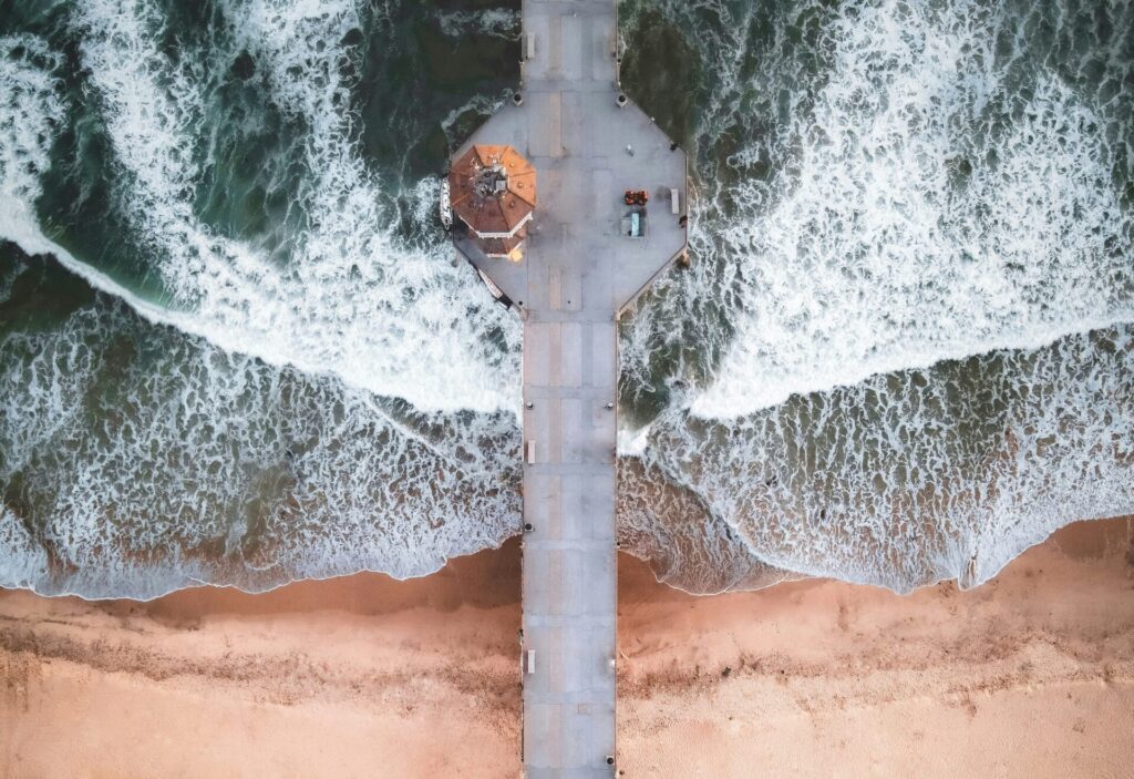 A bird's-eye drone view of Huntington Pier, perfectly symmetrical on both sides, with waves rolling evenly on both sides