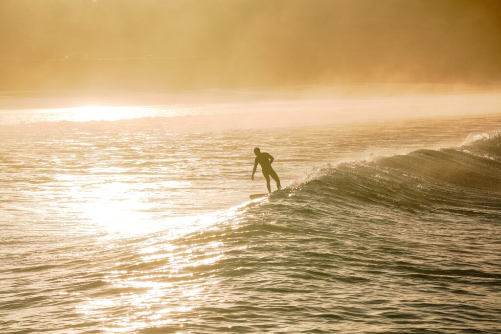 A surfer riding a small wave in the distance, with sunlight reflecting off the water, creating a warm yellow in El Palmar Surf, Spain