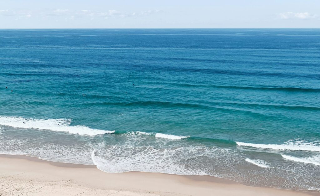 Rolling waves crash against the shore in Praia da Arrifana Surf, Algarve, showcasing vibrant blue water under a clear sky