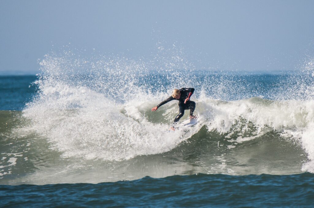 A surfer performs a powerful cutback, carving into a blue wave with a huge spray of water under clear skies in Huntington Beach surf, California