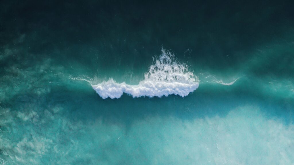 A drone shot of Cocoa Beach surf, Florida, showcasing a single wave breaking in the blue ocean, capturing the beauty of the coastline from above