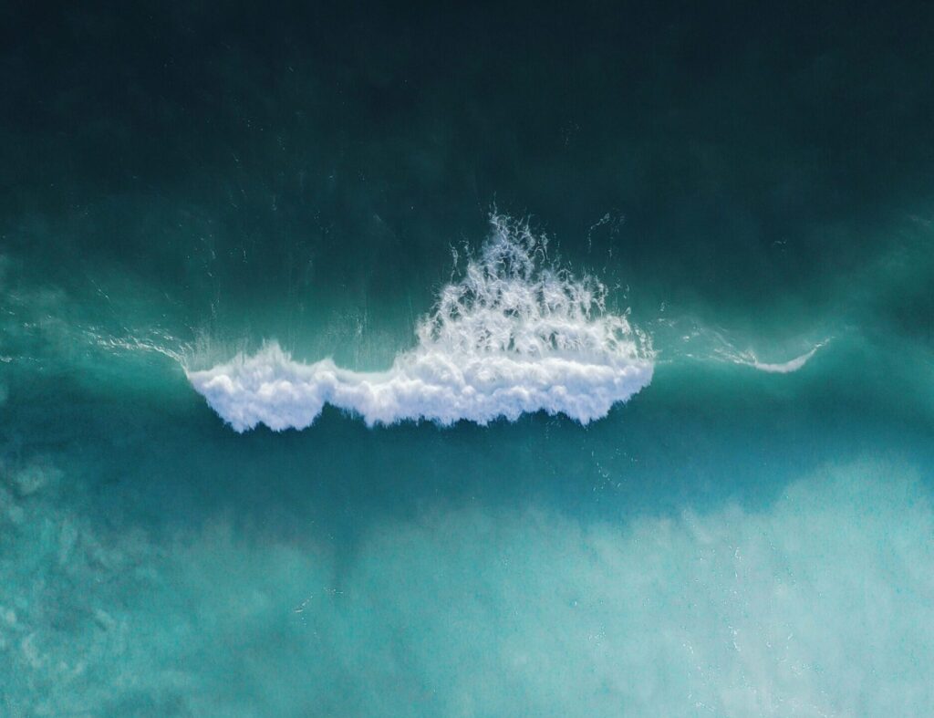 A drone shot of Cocoa Beach surf, Florida, showcasing a single wave breaking in the blue ocean, capturing the beauty of the coastline from above