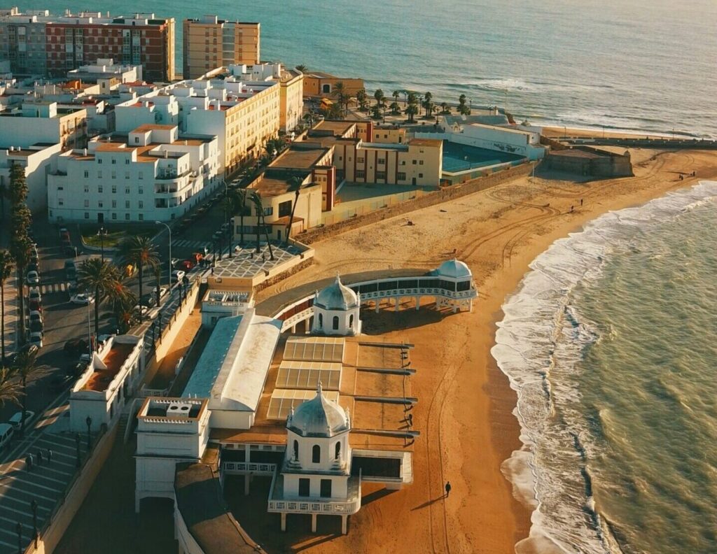 Aerial view of Cadiz, with the town on the left, sandy beaches stretching into the background, and vibrant blue water