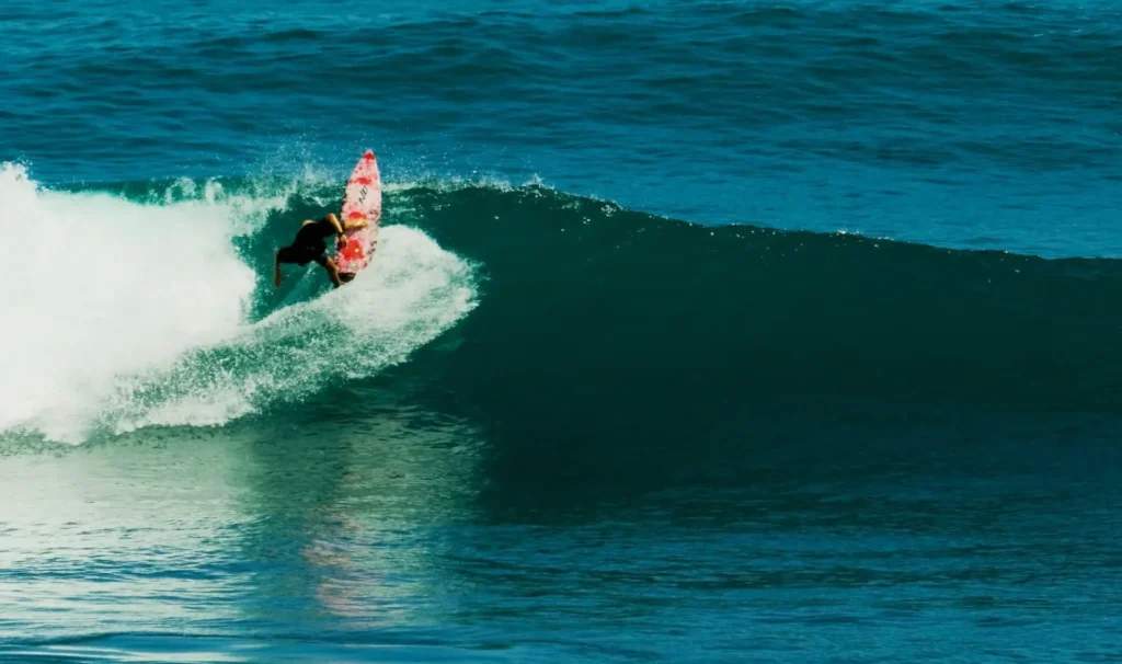 Surfer performs a backside top turn on clean waves with blue water at Uluwatu, Indonesia