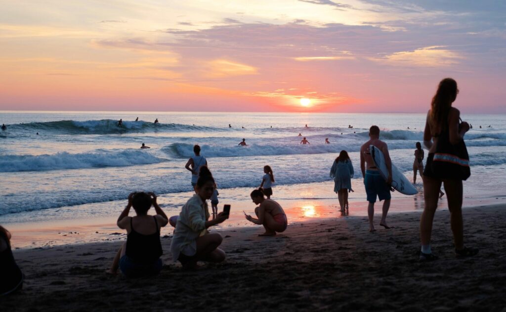 Beach shot at sunset with people on the beach and a surfer on a wave, set against red skies at Canggu Surf, Indonesia