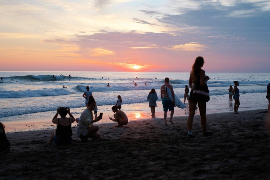 Beach shot at sunset with people on the beach and a surfer on a wave, set against red skies at Canggu, Indonesia