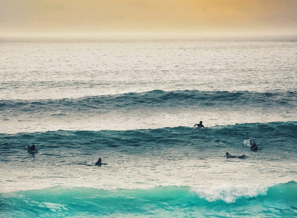 Surfers at Fistral Beach, Newquay surf, with a two-wave set, one paddling into a wave under low sun and yellow skies