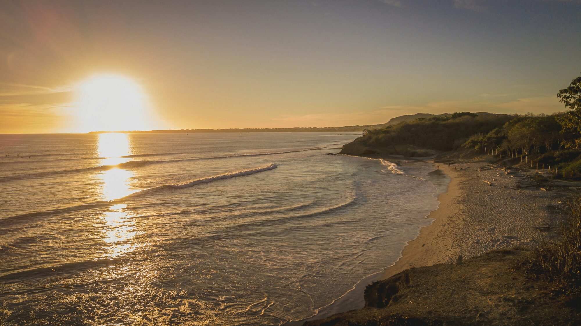 The beach at Playa La Lancha, Mexico, with a setting sun casting a yellow glare over the ocean and sand at Punta Mita surf