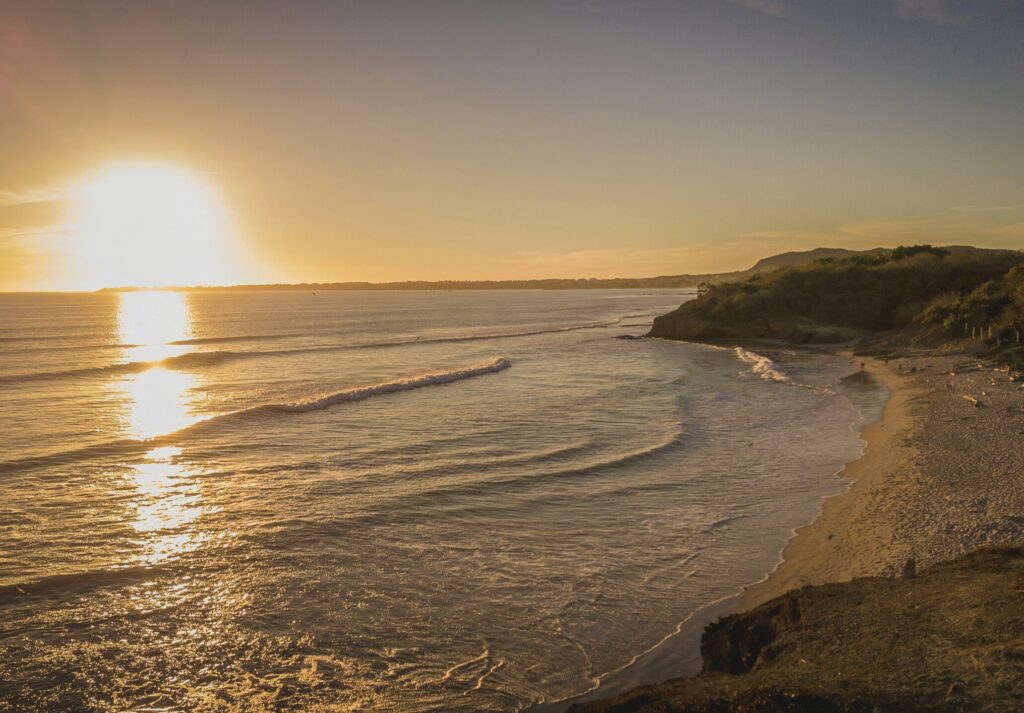 The beach at Playa La Lancha, Mexico, with a setting sun casting a yellow glare over the ocean and sand at Punta Mita surf