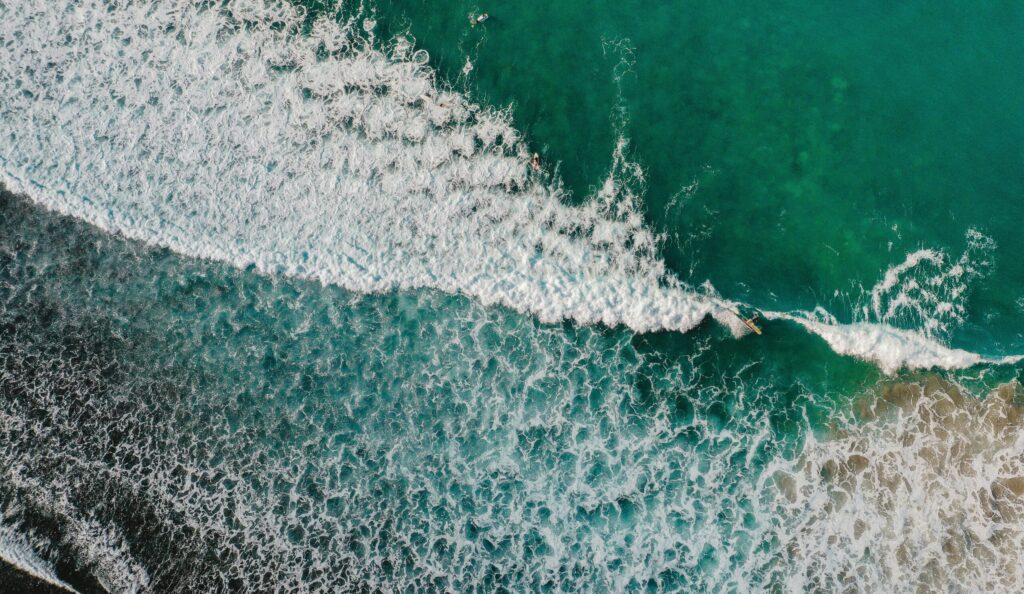 Drone bird's-eye view of Sayulita surf Beach, Mexico, with a wave breaking on a left-hand point, featuring white and blue water