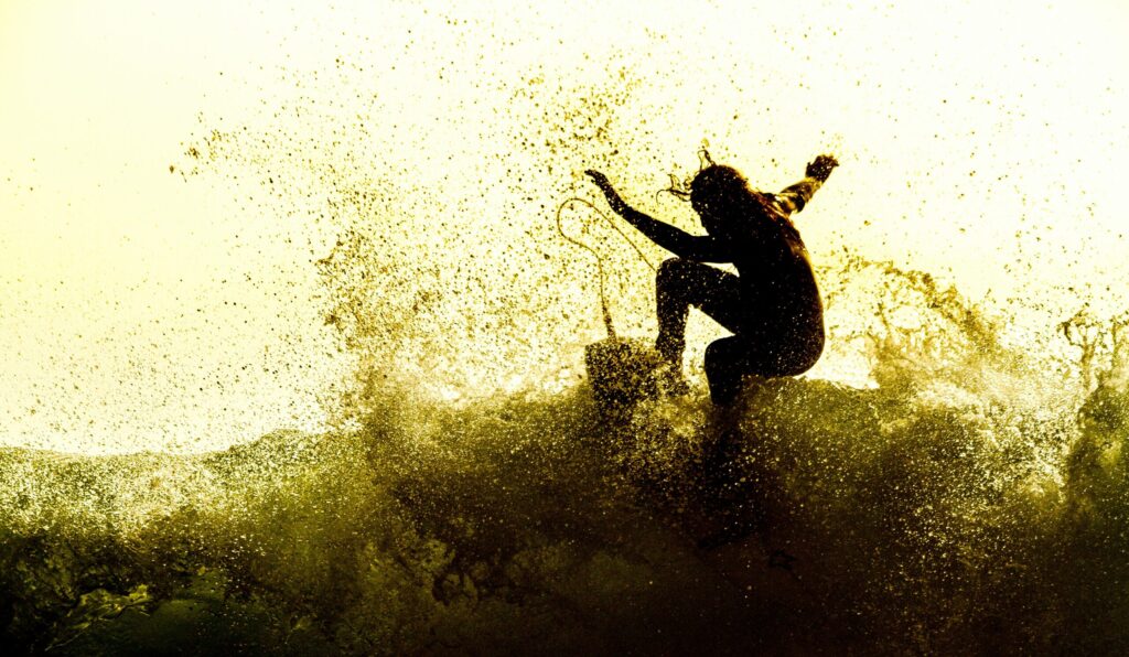 A surfer pulling a turn at Victoria Bay Surf, South Africa, with a yellow tint from the sun and lots of water spray