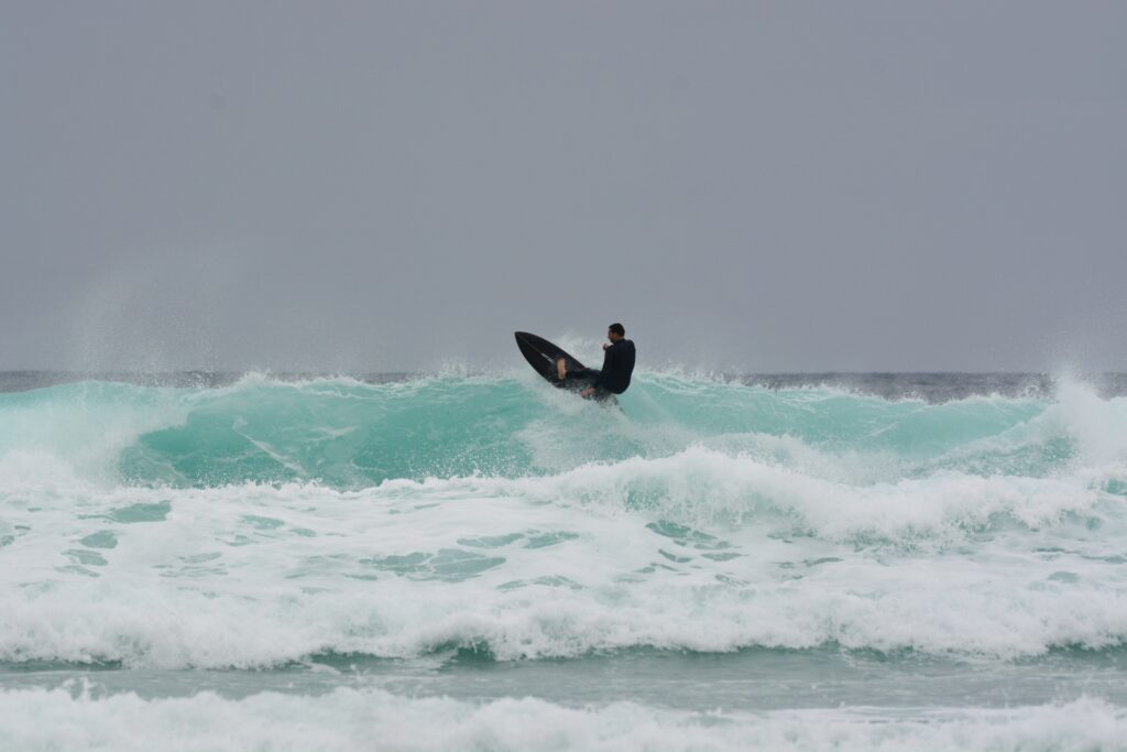 A surfer pulling off a turn on top of the wave at Watergate Bay, Newquay surf, with light blue waters and clear skies