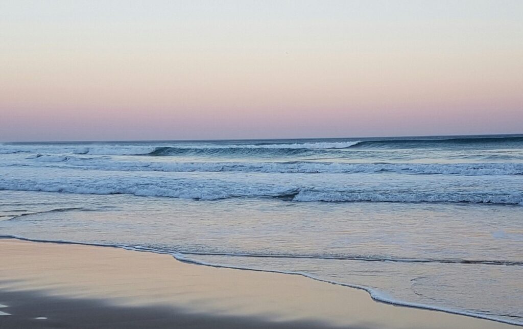 Rolling waves at Wilderness Beach, South Africa Surf, at dusk with low light, blue ocean water, clear skies, and sandy shore