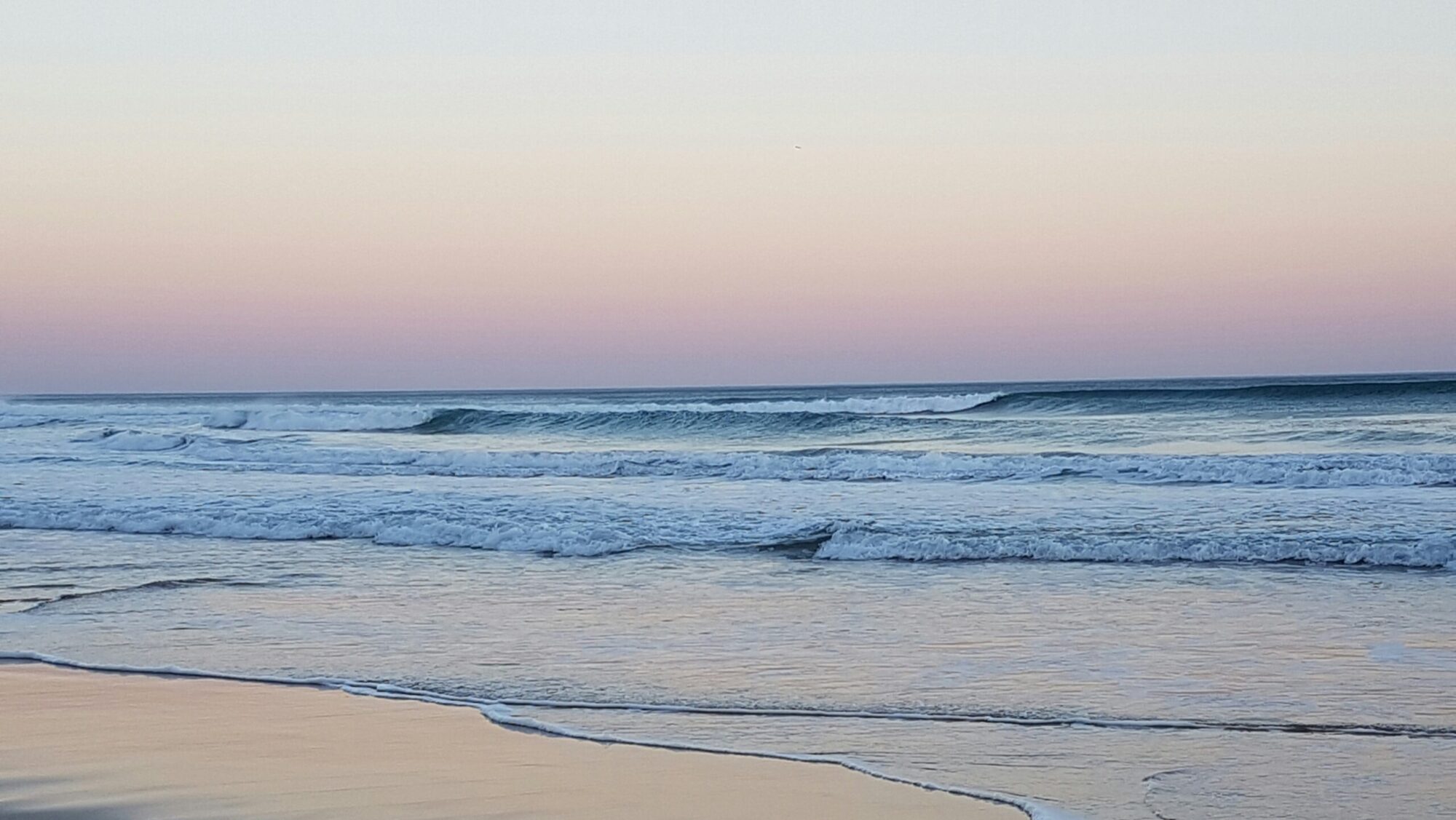 Rolling waves at Wilderness Beach, South Africa Surf, at dusk with low light, blue ocean water, clear skies, and sandy shore