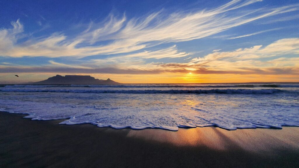 Sunset at Wilderness Beach, South Africa, with yellow and blue skies, wispy clouds, and a view over the ocean from the beach