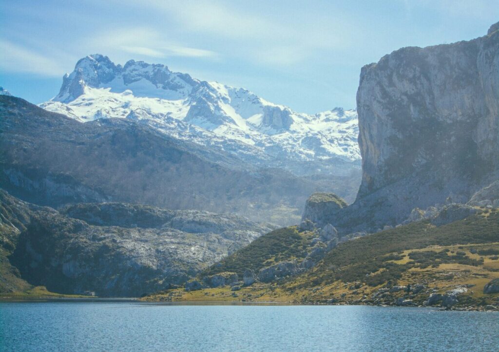 A view of the Lakes of Covadonga in Asturias, featuring snow-capped mountains in the background against a clear blue sky