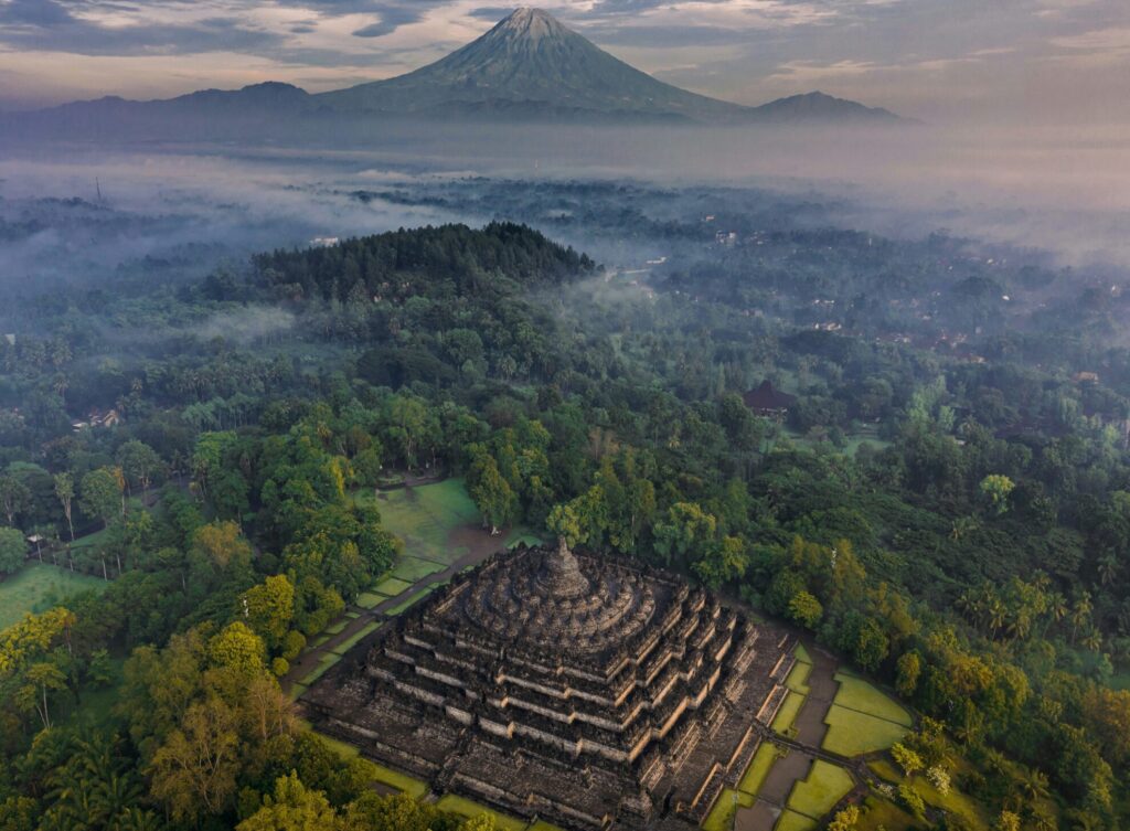 Drone image of Borobudur Temple in Indonesia, with low fog and a mountain in the distance